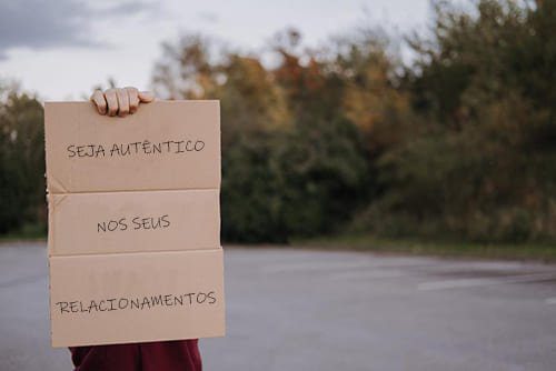 foto de uma pessoa em pé em uma estrada arborizada, com um pedaço de caixa de papelão bege na mão direita, cobrindo sua cabeça e corpo. Nesse tipo de cartaz está escrito seja autêntico em seus relacionamentos. A imagem ilustra o artigo Autenticidade nos Relacionamentos: Medo, Rejeição e Autoconhecimento do blog do Homero Monaco no site Online Psicanalista