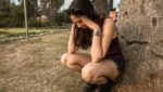 Foto de uma mulher em um parque com shorts e regata pretas. Ela está agachada com as mãos na cabeça, enconstada em uma árvore, como se estivesse tentando se acalmar de um ataque de ansiedade. A foto ilustra o artigo "Psicanalistas que tratam a Ansiedade Desvendam Tabus e Mudam Vidas" escrito por Homero Mônaco para o site Online Psicanalista.
