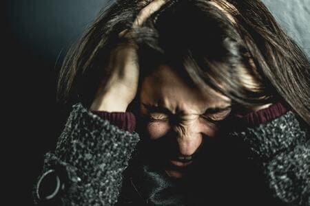 Foto de uma mulher com pullover cinza e com mãoes na cabeça como se estivesse tentando se acalmar de um ataque de ansiedade. A foto ilustra o artigo "Psicanalistas que tratam a Ansiedade Desvendam Tabus e Mudam Vidas" escrito por Homero Mônaco para o site Online Psicanalista.