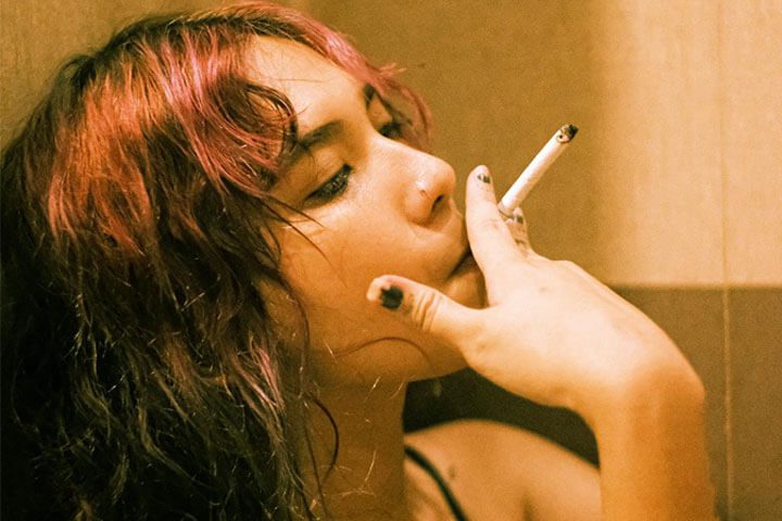 Foto de uma jovem de perfil sentada no chão e apoiada na parede fumando um cigarro. A foto ilustra o artigo 7 maneiras de como a psicanálise vai te ajudar no tratamento da dependência escrito no blog do psicanalista Homero Mônaco para ao site Online Psicanalista.