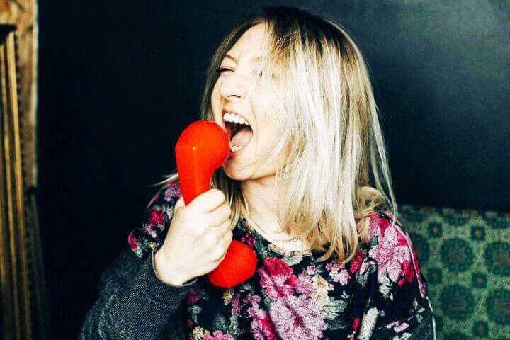 Foto de uma mulher loira, com o gancho do telefone na sua boca, gritando com raiva com a pessoa que está do outro lado da linha. A foto ilustra o artigo Como os Transtornos Psicológicos Influenciam nos seus Relacionamentos escrito pelo psicanalista Homero Mônaco para o site Online Psicanalista.