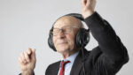 Foto de um homem de uns 60 anos, com fone de ouvido dançando. Ele está de terno e gravata. A foto ilustra o artigo 10 Benefícios da Terapia para a Expansão da sua Consciência Emocional escrito pelo psicanalista Homero Mônaco para o site Online Psicanalista.