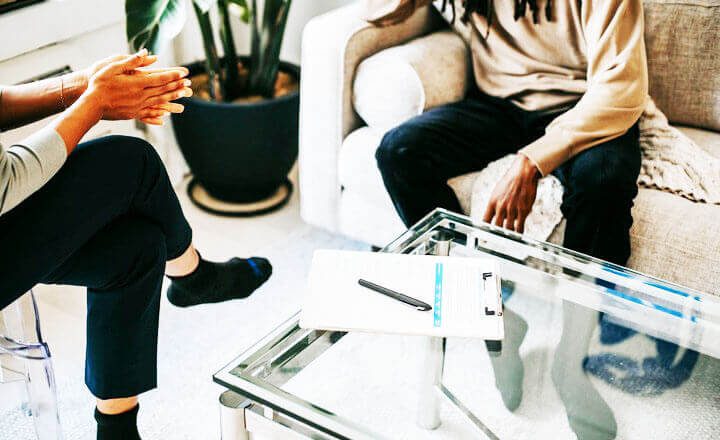 Foto de um homem negro sentado em um sofá bege, enquanto conversa com um terapeuta sentado à sua frente. A foto ilustra o artigo Por que desconstruir os seus padrões comportamentais por meio da sua aceitação e da sua transformação escrito pelo psicanalista Homero Mônaco para o site Online Psicanalista.Foto de uma menina com perna levantada como se fosse pisar na lente da câmera que a fotografa. A foto ilustra o artigo 10 Melhores Maneiras para Construir a Resiliência Emocional com a Psicanálise escrito pelo psicanalista Homero Mônaco para o site Online Psicanalista.