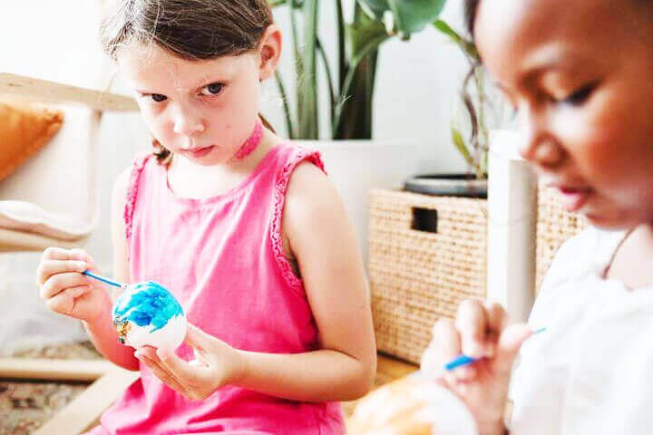 Foto de uma menina sentada em um sofá pintando um ovo que está na sua mão, enquanto olha para outra menina sentada no mesmo sofá, também pintando um ovo. A primeira menina parece estar olhando para aprender com a outra, mas existe um certo olhar de inveja em sua face. A foto ilustra o artigo Por que desconstruir os seus padrões comportamentais por meio da sua aceitação e da sua transformação escrito pelo psicanalista Homero Mônaco para o site Online Psicanalista.Foto de uma menina com perna levantada como se fosse pisar na lente da câmera que a fotografa. A foto ilustra o artigo 75% do seu Comportamento foi Moldado pelas Experiências da sua Infância escrito pelo psicanalista Homero Mônaco para o site Online Psicanalista.